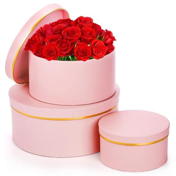 Three pink round boxes adorned with vibrant red roses on top, arranged elegantly.