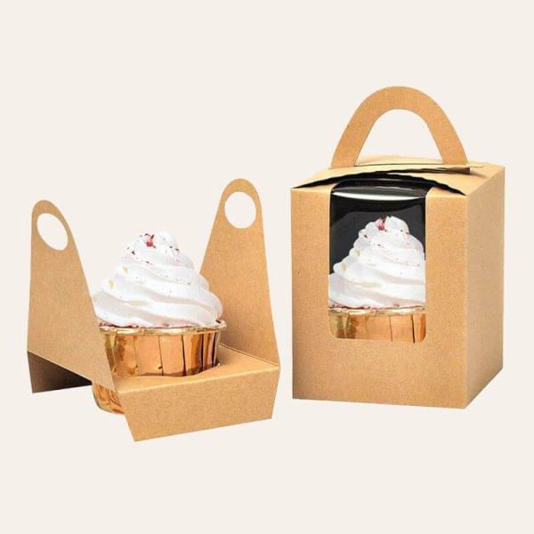 Two colorful cupcakes in a paper box with a handle, ready for transport or gifting.